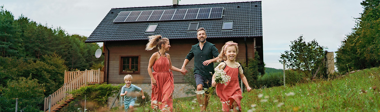 Gl&uuml;ckliche Familie l&auml;uft vor Einfamilienhaus mit Solaranlage im Garten und steht f&uuml;r erneuerbare Energien in Wiesbaden nachhaltig.