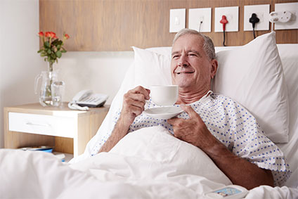 Älterer Mann liegt in einem Krankenhausbett und trinkt einen Tee