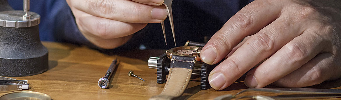 Ein Mann der mit verschiedenen Werkzeugen eine Uhr repariert.