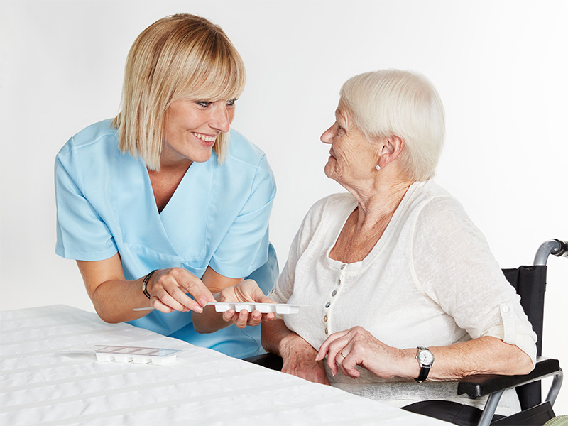 Pflegekraft gibt älterer Frau Tabletten – fürsorgliche Betreuung im Alter und medizinische Unterstützung zu Hause