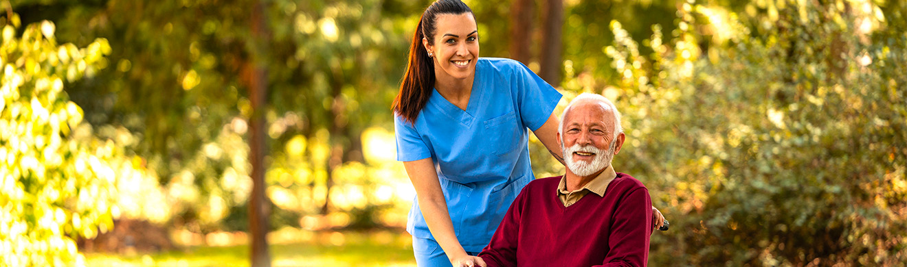 Pflegekraft unterstützt älteren Mann im Rollstuhl draußen im Park, symbolisch für stationäre Pflege in Wiesbaden.
